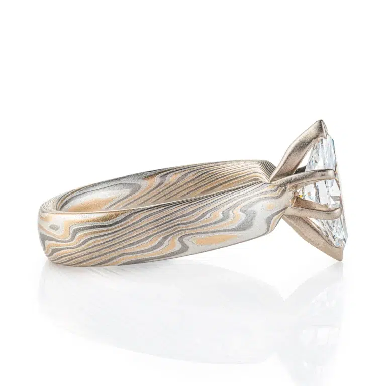 ring with a solitaire stone set in prongs, featuring marquise shaped white stone, band portion is made with yellow gold, palladium and sterling silver