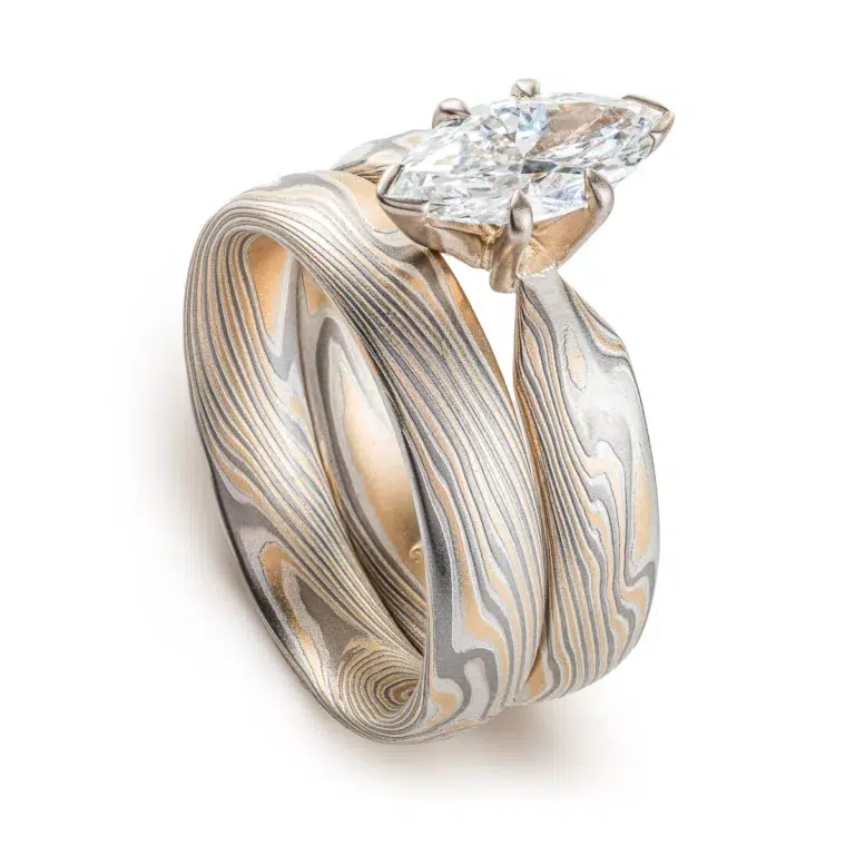 pair of stacked rings patterned in mokume twist style, the ring on top has a single marquise shaped diamond, that is wider than the band it is on and hangs over the front of the band underneath it