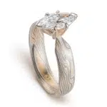 ring with a solitaire stone set in prongs, featuring marquise shaped white stone, band portion is made with yellow gold, palladium and sterling silver