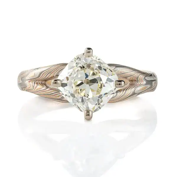 mokume ring with large cushion shaped diamond held in prongs, the band part of the ring is split into a y shape leading into the stone on either side