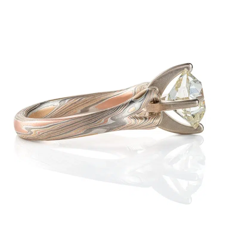 mokume ring with large cushion shaped diamond held in prongs, the band part of the ring is split into a y shape leading into the stone on either side