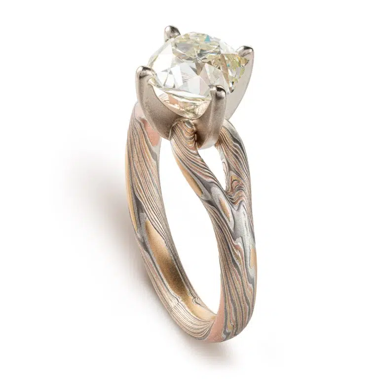 mokume ring with large cushion shaped diamond held in prongs, the band part of the ring is split into a y shape leading into the stone on either side