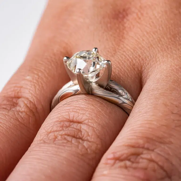 mokume ring with large cushion shaped diamond held in prongs, the band part of the ring is split into a y shape leading into the stone on either side
