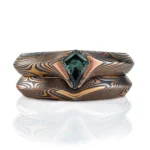 pair of mokume gane rings nested together, stacked one on top of the other, one with a kite shaped green stone set into it