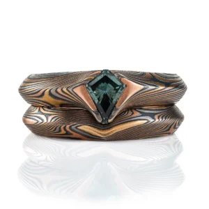 pair of mokume gane rings nested together, stacked one on top of the other, one with a kite shaped green stone set into it