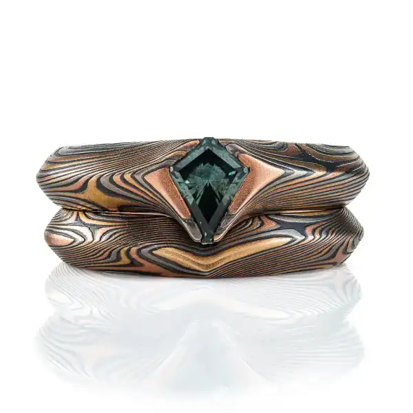 pair of mokume gane rings nested together, stacked one on top of the other, one with a kite shaped green stone set into it
