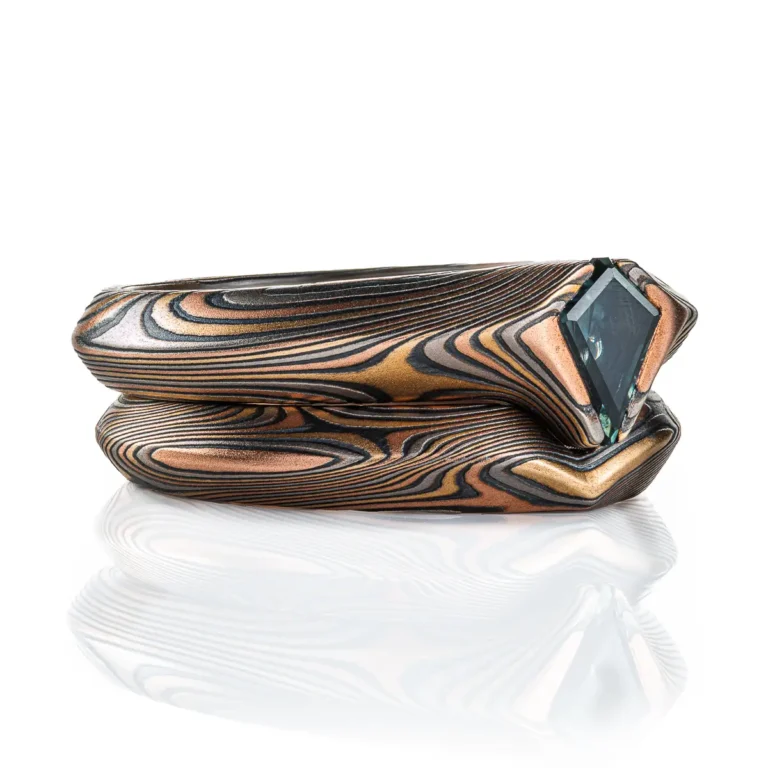 pair of mokume gane rings nested together, stacked one on top of the other, one with a kite shaped green stone set into it