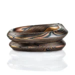 pair of mokume gane rings nested together, stacked one on top of the other, one with a kite shaped green stone set into it