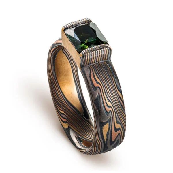 mokume gane ring with multicolored layers of metals, with a large dark green stone set into it