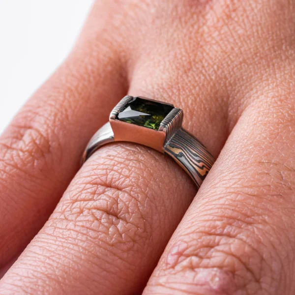 mokume gane ring with multicolored layers of metals, with a large dark green stone set into it