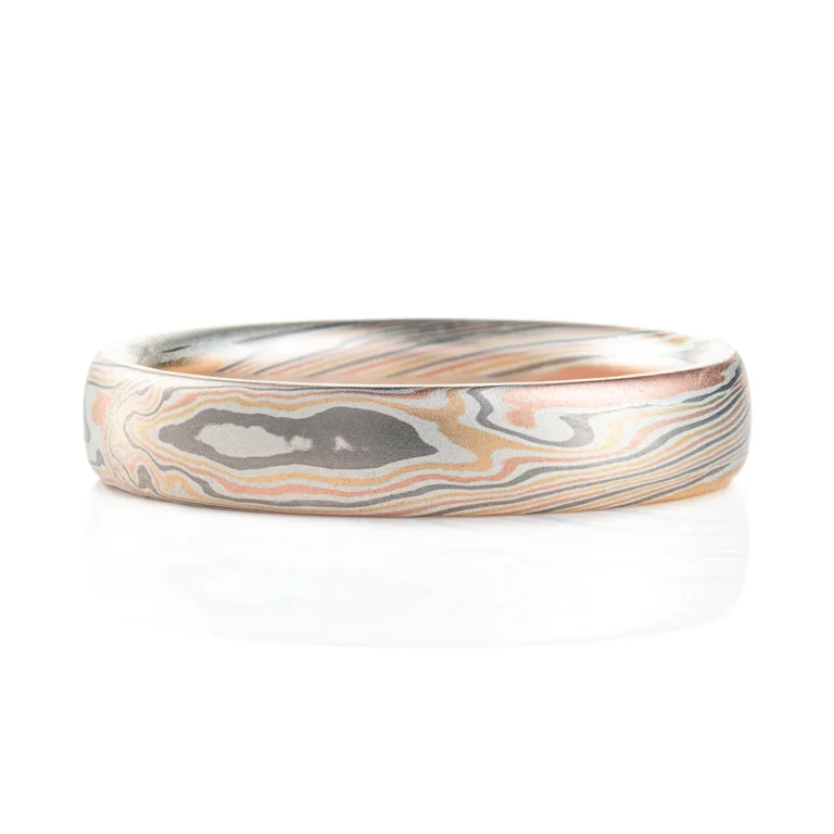 Classic narrow wedding band in a mokume twist pattern, with a domed profile and smooth surface, made with layers of red gold, silver, palladium and yellow gold.