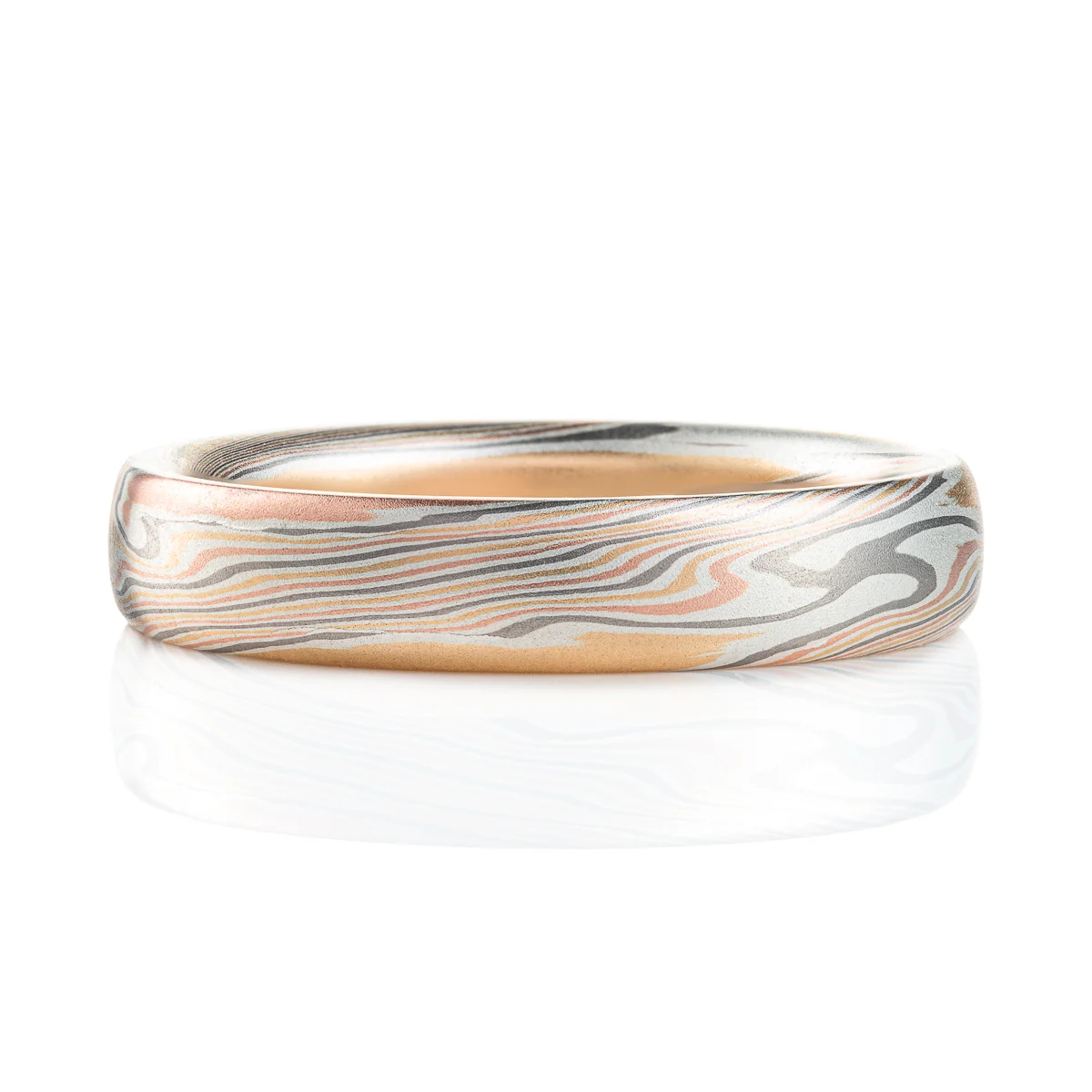 Classic narrow wedding band in a mokume twist pattern, with a domed profile and smooth surface, made with layers of red gold, silver, palladium and yellow gold.