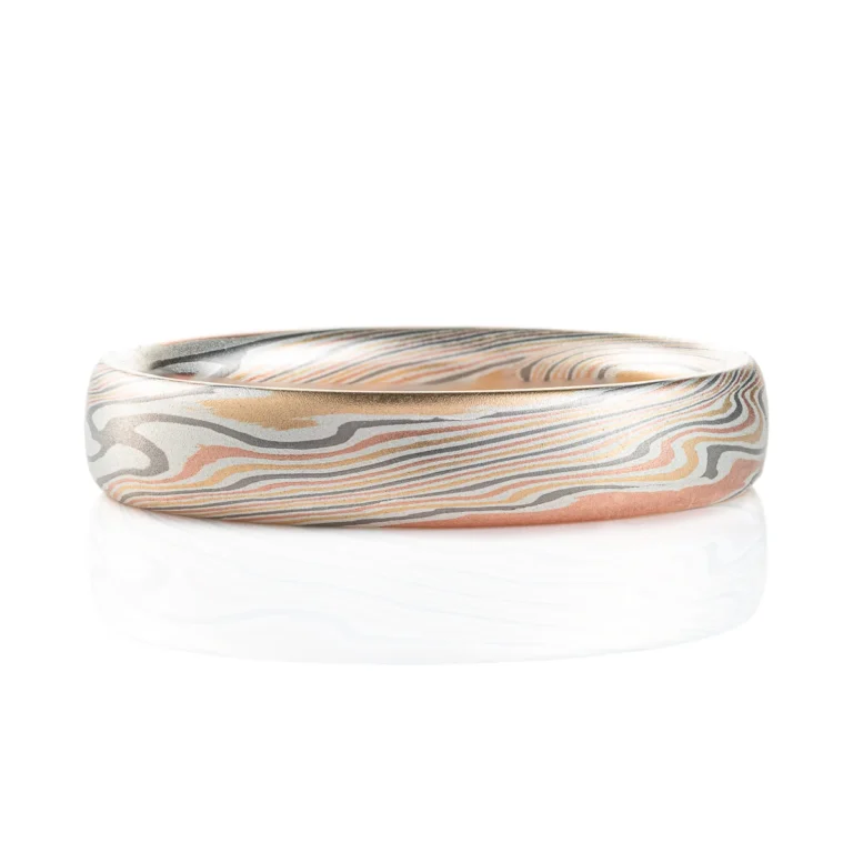 Classic narrow wedding band in a mokume twist pattern, with a domed profile and smooth surface, made with layers of red gold, silver, palladium and yellow gold.