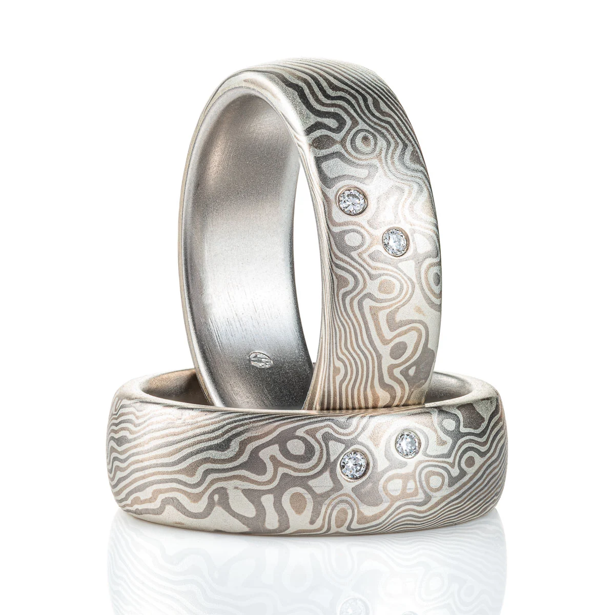 This beautiful Mokume Gane ring set has the perfect celestial vibe. These matching rings are shown in the combo Twist/Droplet pattern and Smoke Palette, with a low dome profile, and a satin finish. The Smoke palette features a three metal combination of 14k White Gold, Palladium, and Sterling Silver. These rings also each have two small diamonds set into the droplets of the pattern to create the effect of stars twinkling.