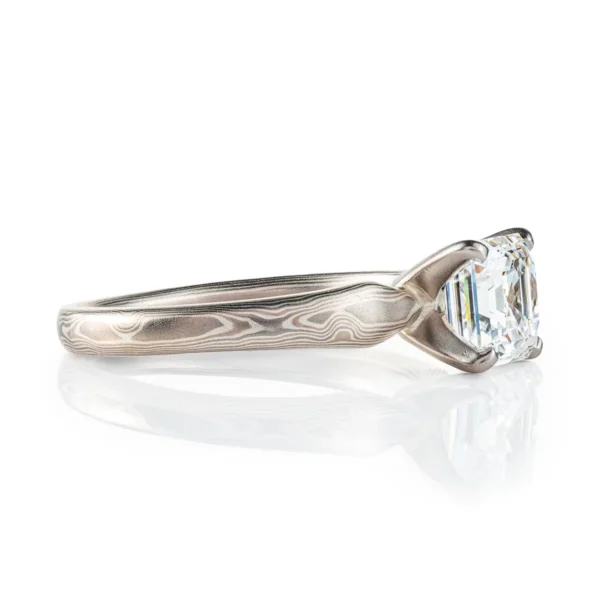 solitaire style mokume gane narrow band in subtle woodgrain pattern, with a prong set square stone