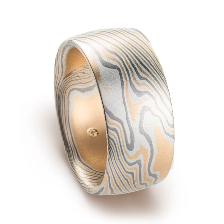 extra wide mokume gane band made in twisted pattern and a combination of yellow gold, palladium and silver, with a low domed profile and smooth finish