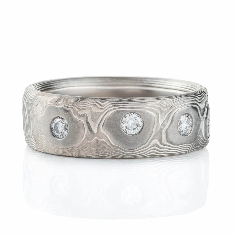 Wide men's style mokume gane band with flush set diamonds scattered around the entire ring for added sparkle. Ring is made in silver and palladium with a textured pattern resembling topography.