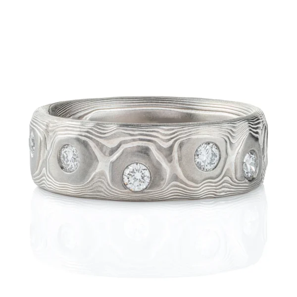 Wide men's style mokume gane band with flush set diamonds scattered around the entire ring for added sparkle. Ring is made in silver and palladium with a textured pattern resembling topography.