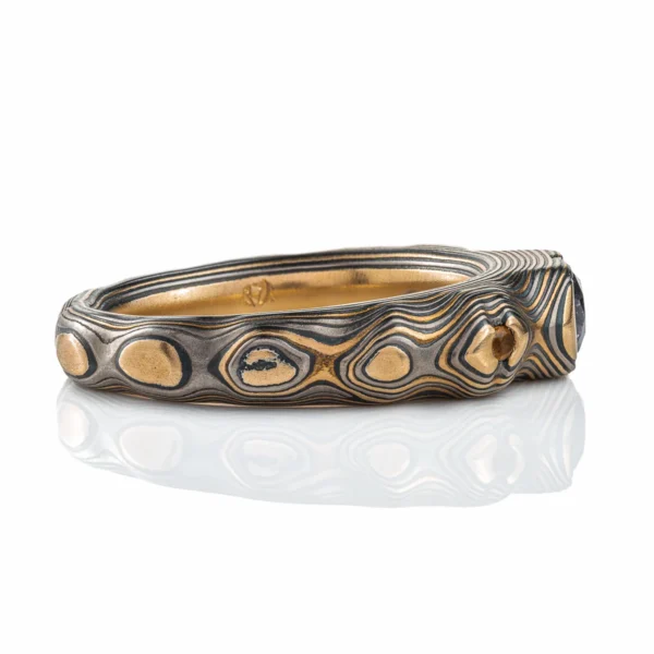 Elegant mokume gane ring with a cathedral style setting, three stones, one larger oval shaped stone at the center, and slightly smaller round stones on either side. Ring is patterned in style made to resemble mountainous terrain.