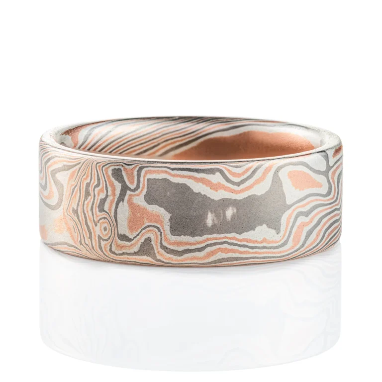 Large, wide mokume ring with bold twist style patterning running diagonally across, with a flat profile and smooth finish. Made with alternating layers of red gold, silver and palladium.