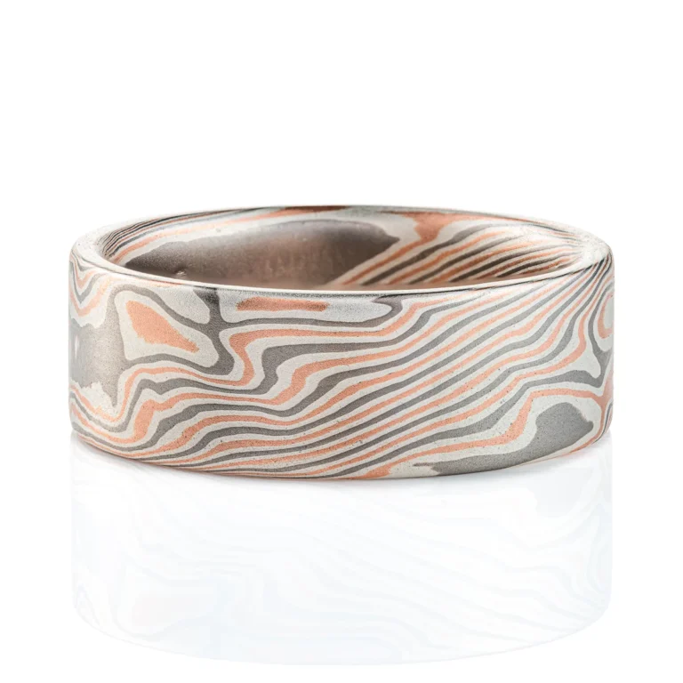 Large, wide mokume ring with bold twist style patterning running diagonally across, with a flat profile and smooth finish. Made with alternating layers of red gold, silver and palladium.