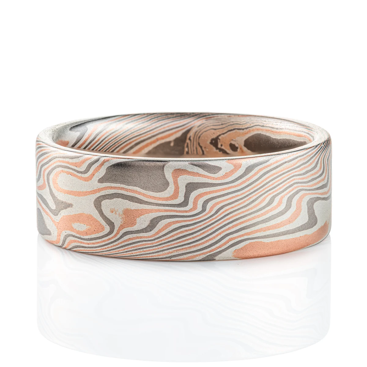 Large, wide mokume ring with bold twist style patterning running diagonally across, with a flat profile and smooth finish. Made with alternating layers of red gold, silver and palladium.