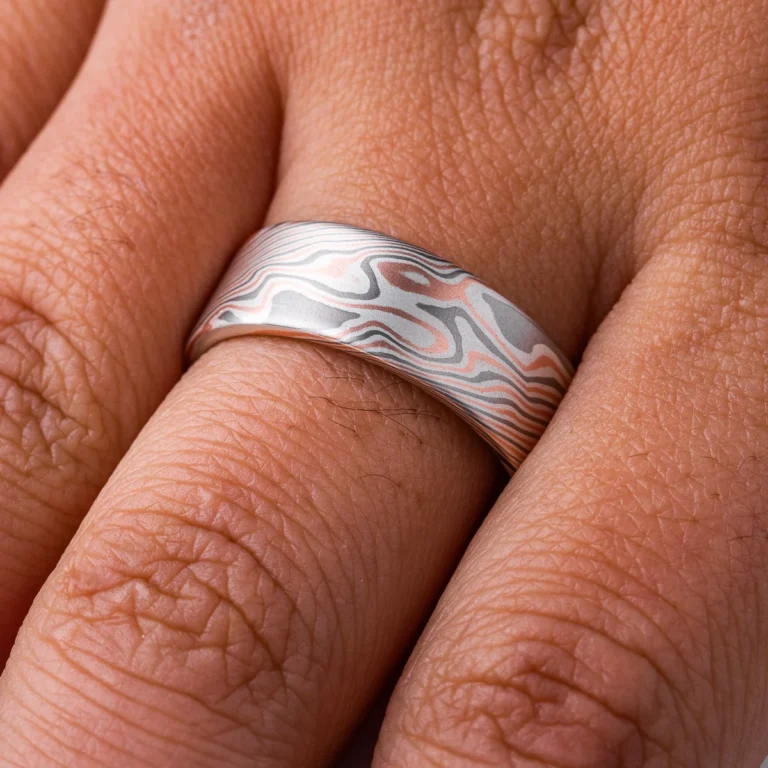 Large, wide mokume ring with bold twist style patterning running diagonally across, with a flat profile and smooth finish. Made with alternating layers of red gold, silver and palladium.