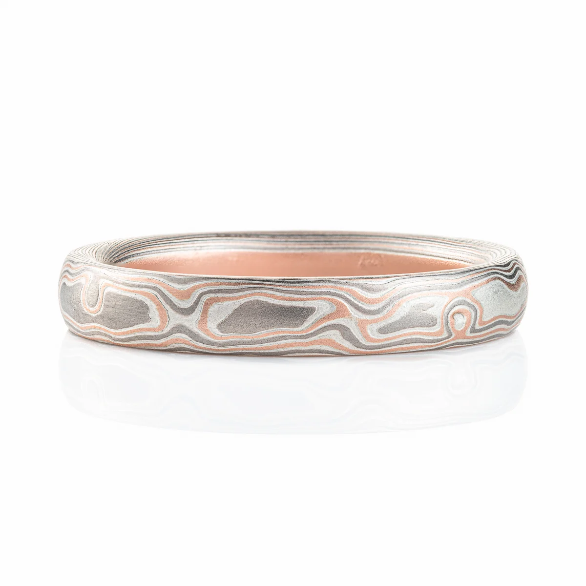 Light feeling narrow wedding band, made in a mokume woodgrain pattern with layers of red gold, palladium and silver, with a slight texture from an etched finish.