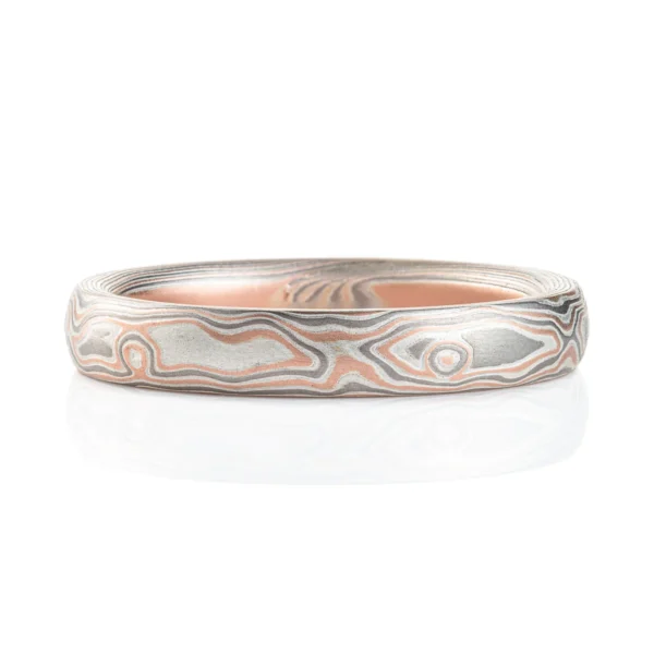 Light feeling narrow wedding band, made in a mokume woodgrain pattern with layers of red gold, palladium and silver, with a slight texture from an etched finish.