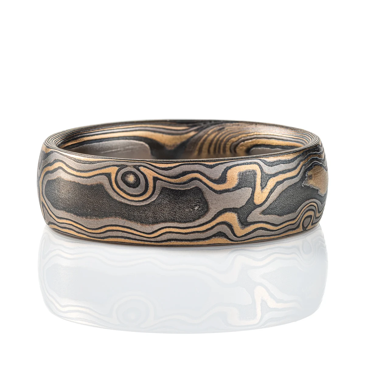 Gold and black mokume gane ring made in classic woodgrain pattern, metal colors used in the ring are yellow gold, palladium and oxidized silver (black in color). The ring has a low dome profile shape and slight texture from an etched finish.