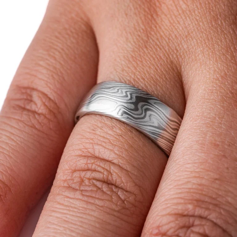 mokume gane band in silvery palette with different shades of gray, made in a twisting pattern and a smooth finish.
