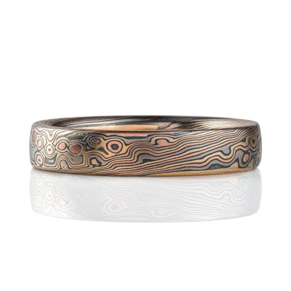 Rustic feeling mokume gane band, narrow width, dark warm toned colors in a swirling mixed pattern.