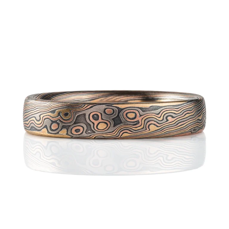 Rustic feeling mokume gane band, narrow width, dark warm toned colors in a swirling mixed pattern.