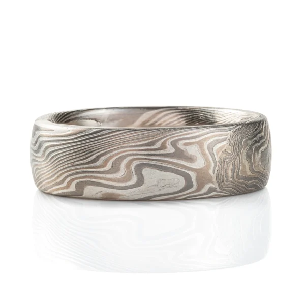 This domed band is patterned in the mokume gane twist style, in a silvery white metal combination, with one blue round stone set flush into the band.