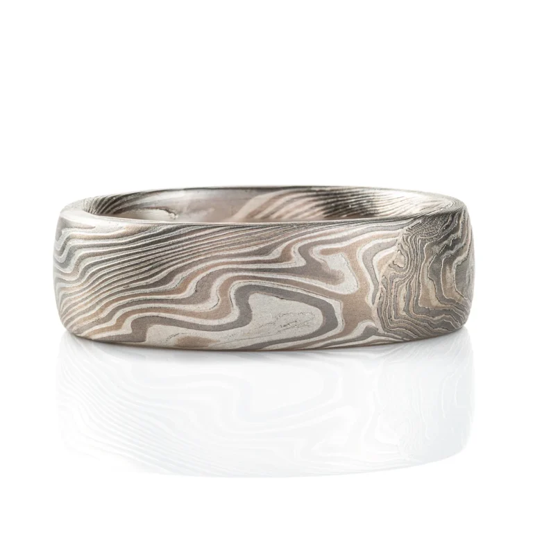 This domed band is patterned in the mokume gane twist style, in a silvery white metal combination, with one blue round stone set flush into the band.