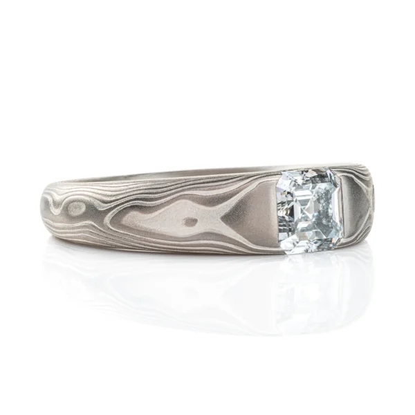 Cathedral style ring with a single diamond set into it, the stone is a soft square shape, the band is light gray and silver in color and tapers towards the underside of the ring.