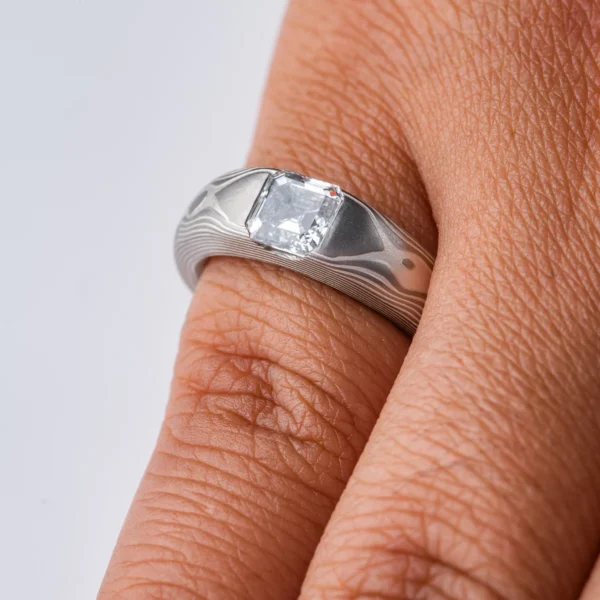 Cathedral style ring with a single diamond set into it, the stone is a soft square shape, the band is light gray and silver in color and tapers towards the underside of the ring.