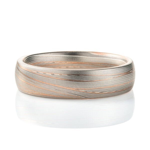 Domed band patterned in mokume style with long thin lines flowing around the ring, made of layers of light and darker gray silver metal, with two layers of red gold added.