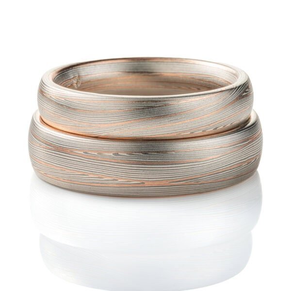 Domed band patterned in mokume style with long thin lines flowing around the ring, made of layers of light and darker gray silver metal, with two layers of red gold added.