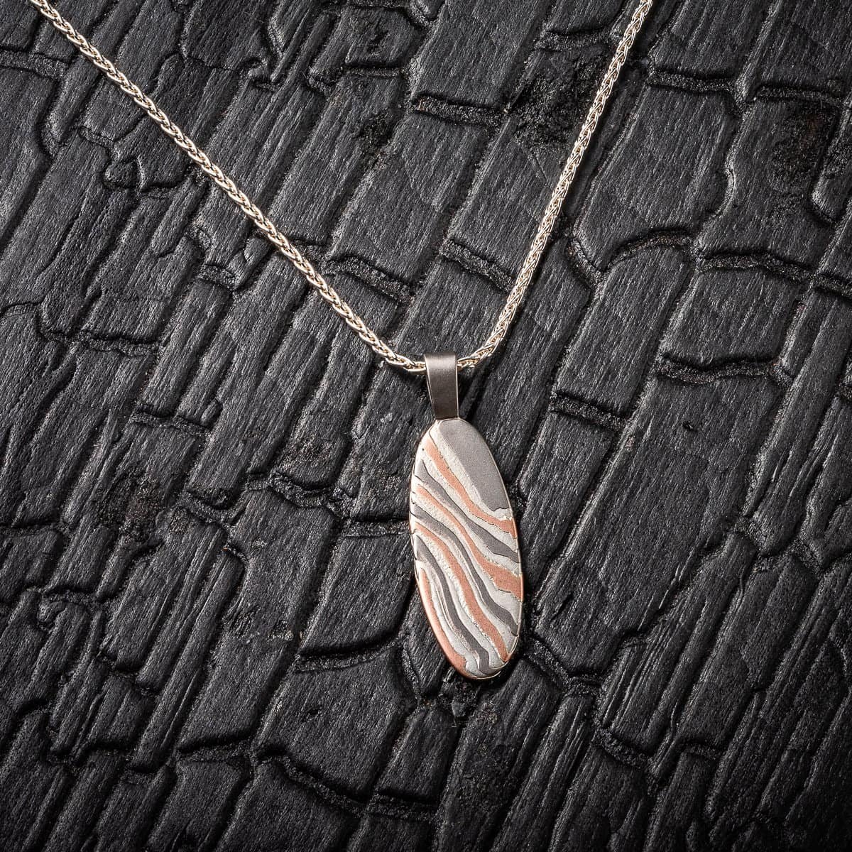 This simple and beautiful mokume gane pendant is made with 14kt red gold, palladium and sterling silver, on a silver chain and with an etched finish.