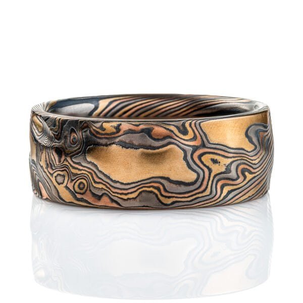 Textured mokume gane band, with carving on the surface to create a rippling effect in relief, similar to rolling hills on a topographic map. Made with layers of red gold, yellow gold, palladium, and silver that has been oxidized to turn it black in color.