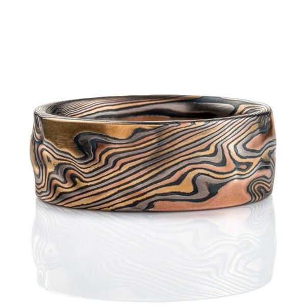 Textured mokume gane band, with carving on the surface to create a rippling effect in relief, similar to rolling hills on a topographic map. Made with layers of red gold, yellow gold, palladium, and silver that has been oxidized to turn it black in color.