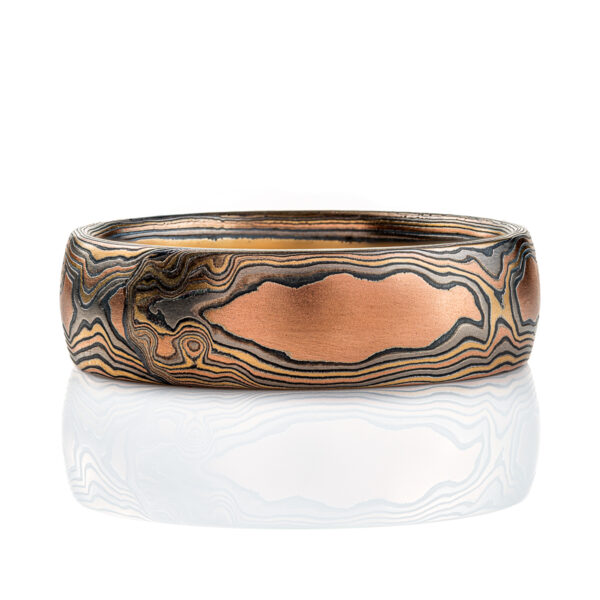 Wide men's style mokume gane band with a domed profile, made in a woodgrain style pattern to resemble wood, with layers of red gold and yellow gold alternating with oxidized silver (black). .