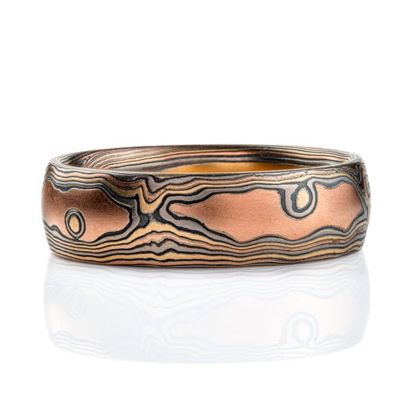 Wide men's style mokume gane band with a domed profile, made in a woodgrain style pattern to resemble wood, with layers of red gold and yellow gold alternating with oxidized silver (black). .