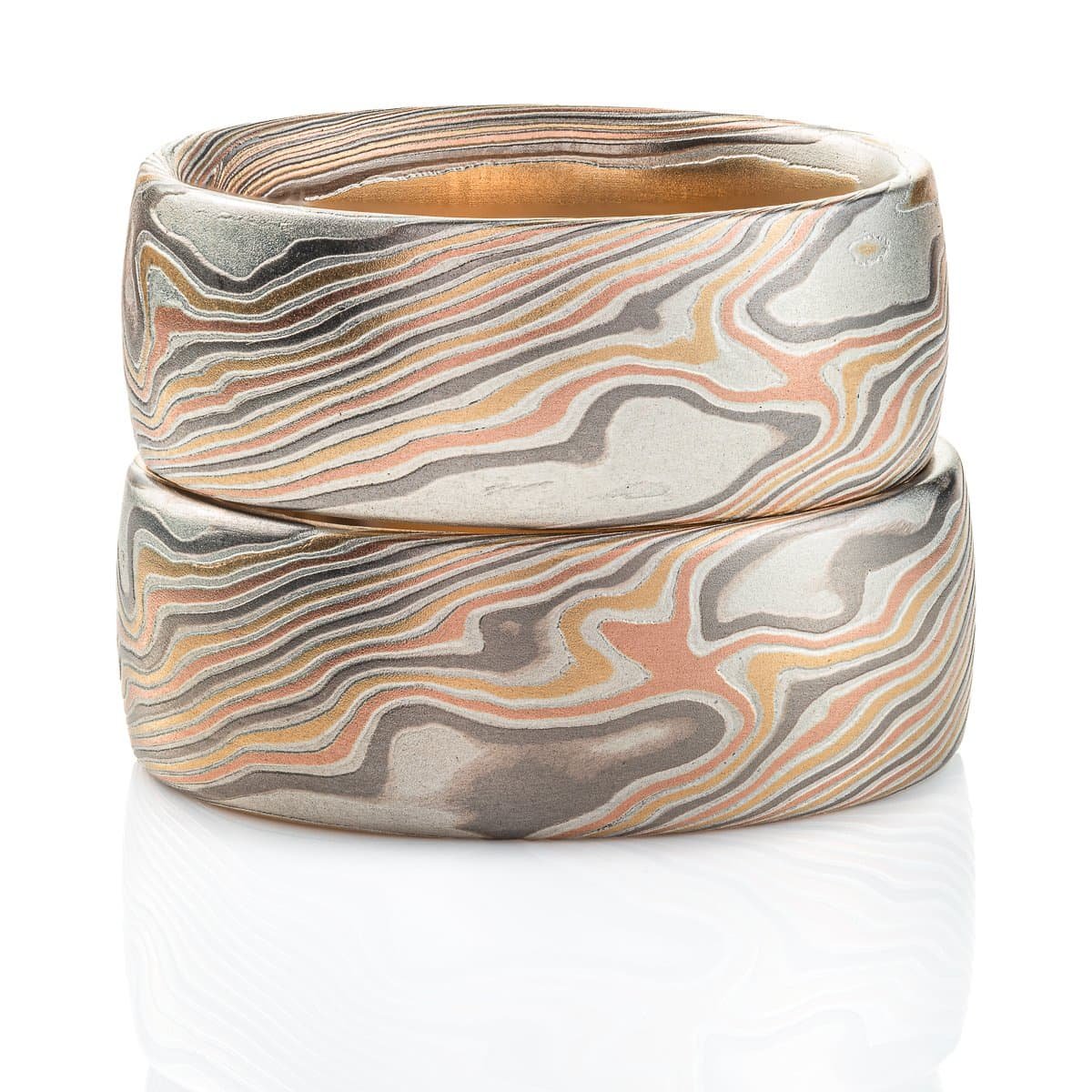 Two mokume gane rings, made in matching pattern and color combinations, with the same widths and similar ring sizes. Both rings made with red gold, yellow gold, palladium and silver.