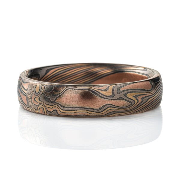 Mokume gane patterned ring, medium width, made in mixture of golds and dark gray metal in a twisting, swooping pattern.