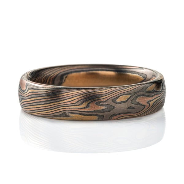 Mokume gane patterned ring, medium width, made in mixture of golds and dark gray metal in a twisting, swooping pattern.