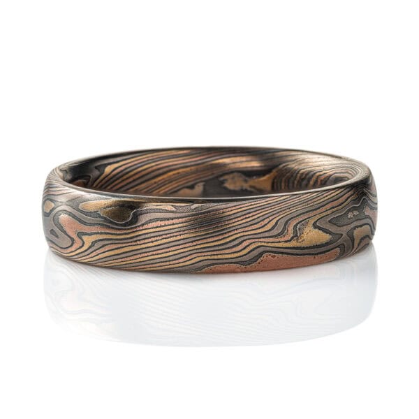 Mokume gane patterned ring, medium width, made in mixture of golds and dark gray metal in a twisting, swooping pattern.