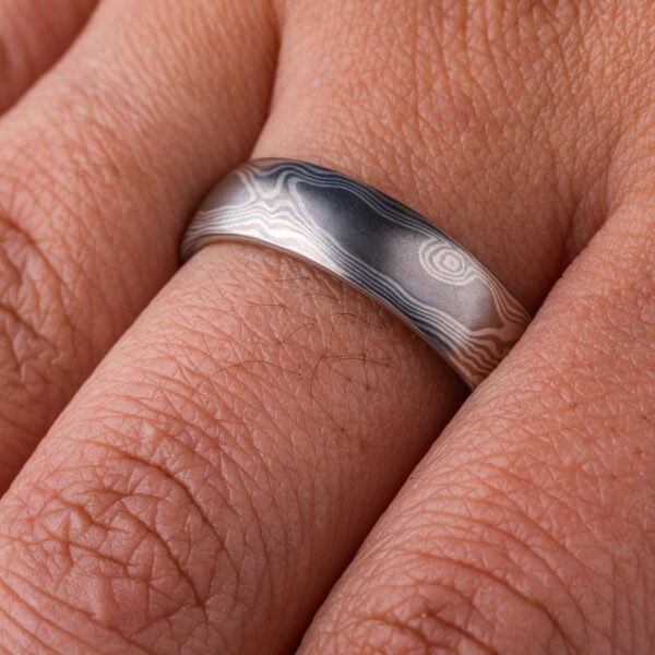 Silvery mokume gane ring made with layers of lighter and darker gray metals, pattern made to look like wood grain.