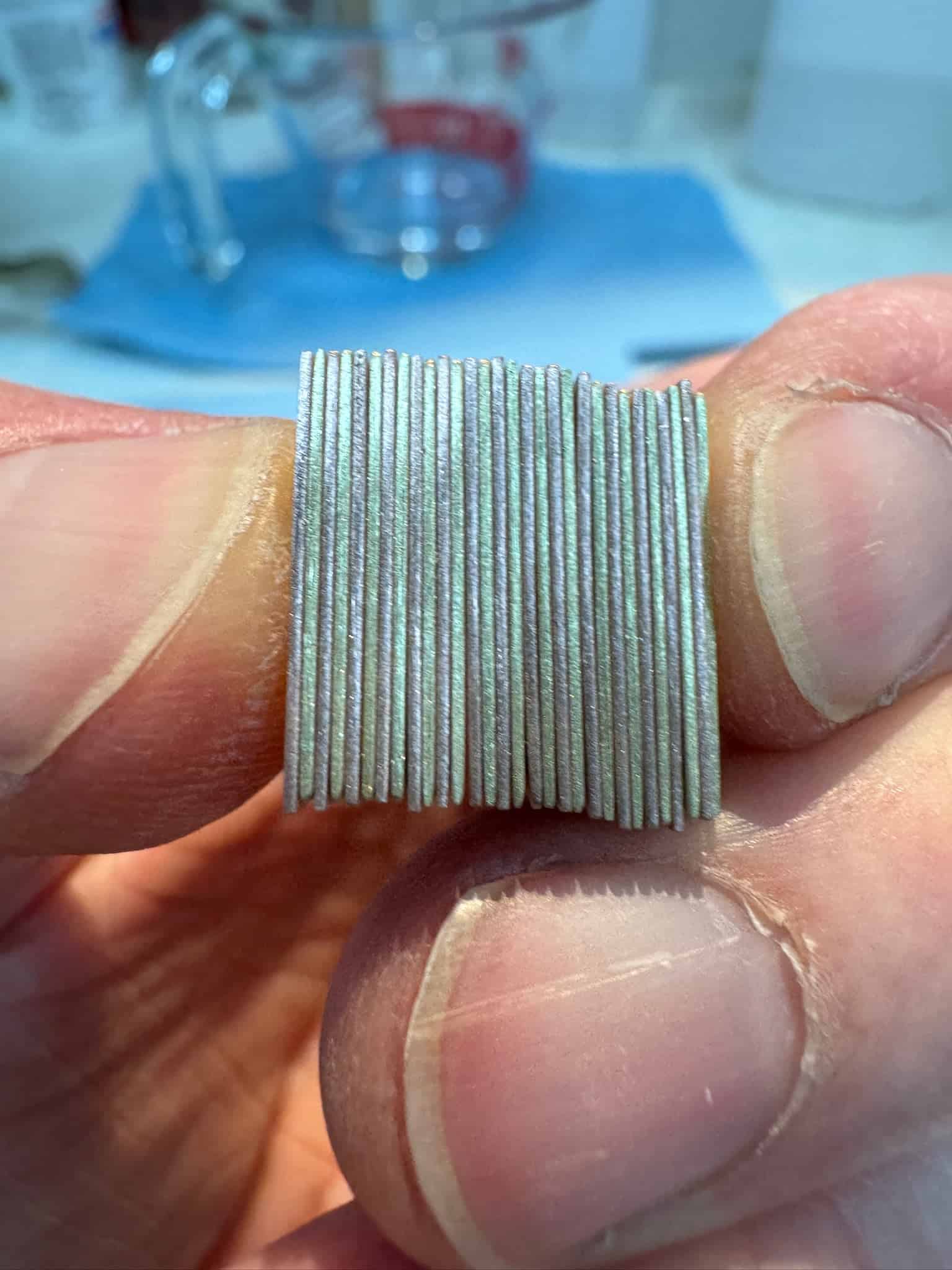 Close up of hand holding a stack of thin metal sheets. The sheets are red and yellow golds.